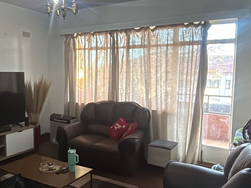 A living room featuring a large window with curtains and a glass door leading to an outdoor area, providing natural light.