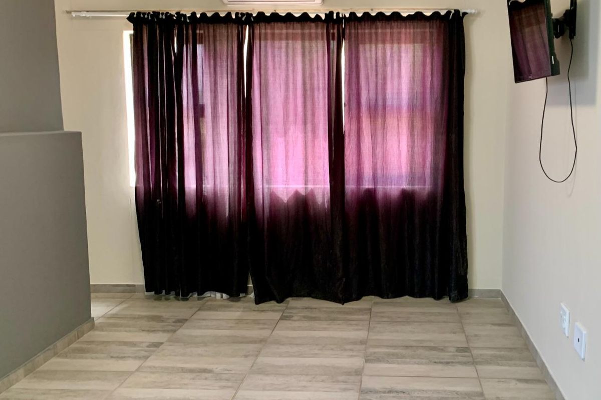 A living area featuring tiled flooring, a wall-mounted air conditioning unit, and a wall-mounted television bracket.