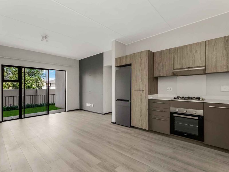 Modern open-plan living area featuring light laminate flooring, a sleek kitchen with built-in appliances, and sliding doors leading to an outdoor space.