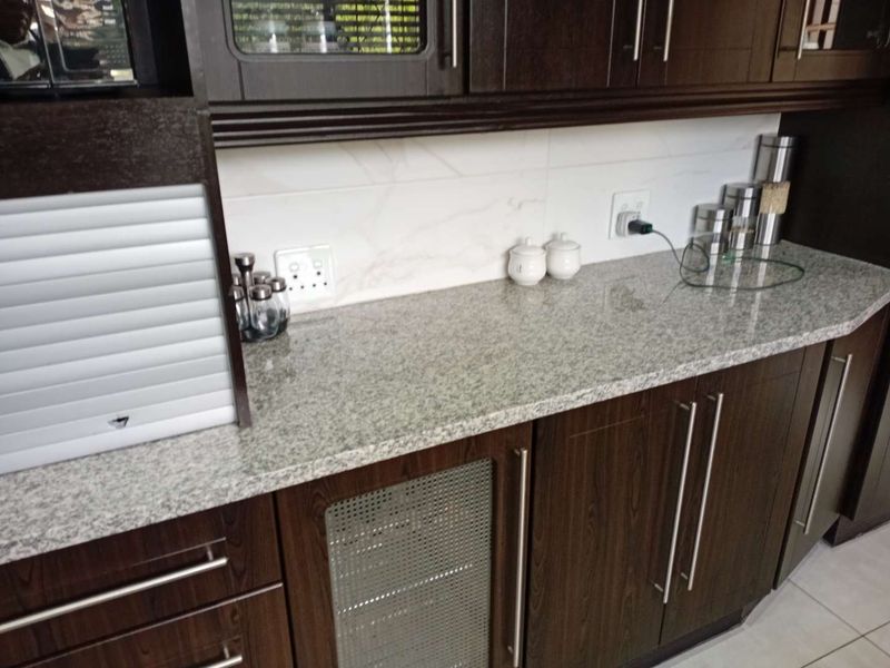 A well-maintained kitchen area featuring dark wood cabinetry, granite countertops, and a clean tiled backsplash with integrated appliance storage.
