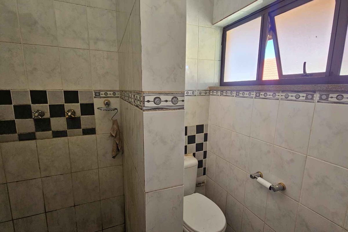 A functional bathroom featuring a shower, toilet, and tiled walls with a top-hung window for ventilation.