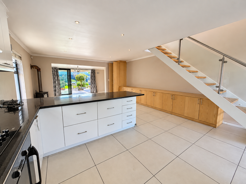 Spacious open-plan kitchen and living area featuring modern cabinetry, a central island, tiled floors, and a sleek staircase leading to the upper level.