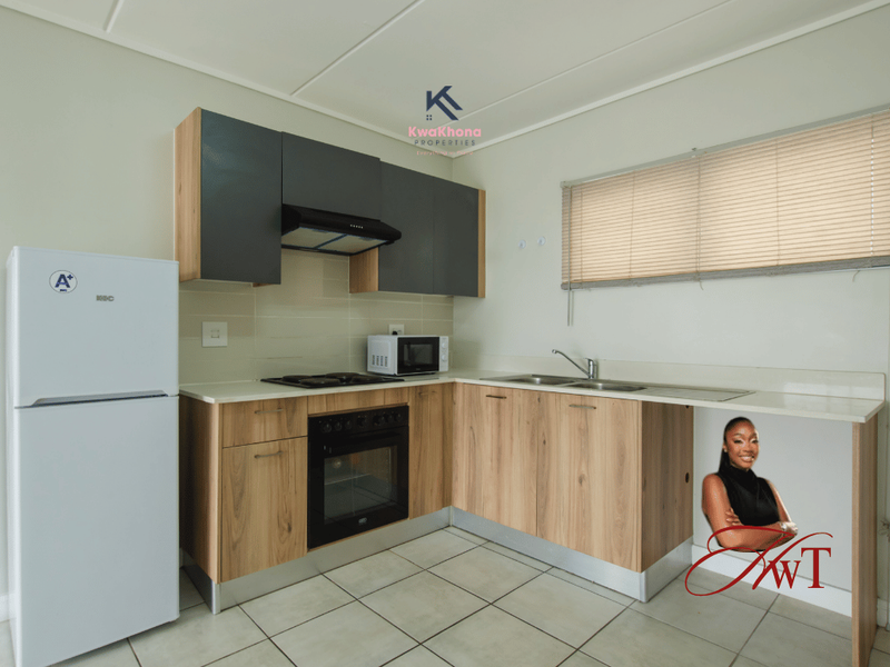 Modern kitchen featuring wood-finish cabinetry, integrated oven and hob, stainless steel sink, and neutral tiled flooring with ample counter space.