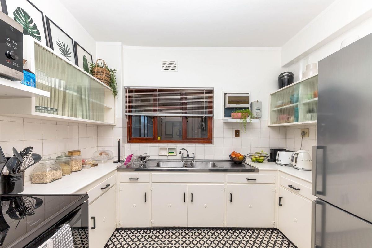 A functional kitchen featuring white cabinetry, a double basin stainless steel sink, tiled backsplash, and distinctive patterned floor tiles.