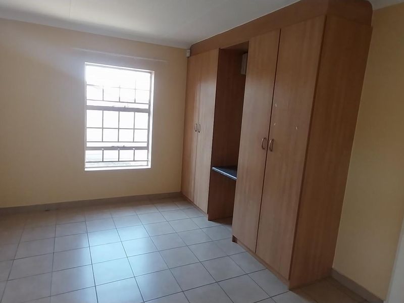 A clean, empty bedroom featuring tiled flooring and built-in wooden cupboards with an integrated desk space.