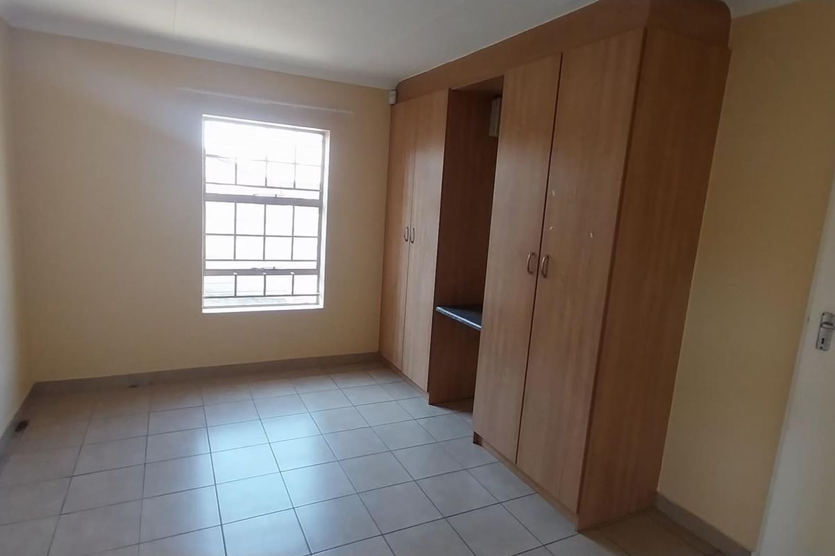 A clean, empty bedroom featuring tiled flooring and built-in wooden cupboards with an integrated desk space.