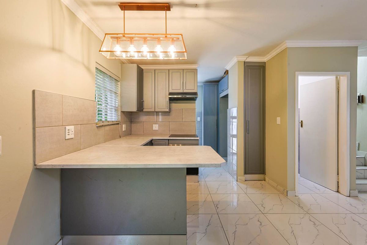 Modern kitchen featuring grey cabinetry, stone-look countertops, tiled flooring, and a breakfast bar, complemented by contemporary pendant lighting.