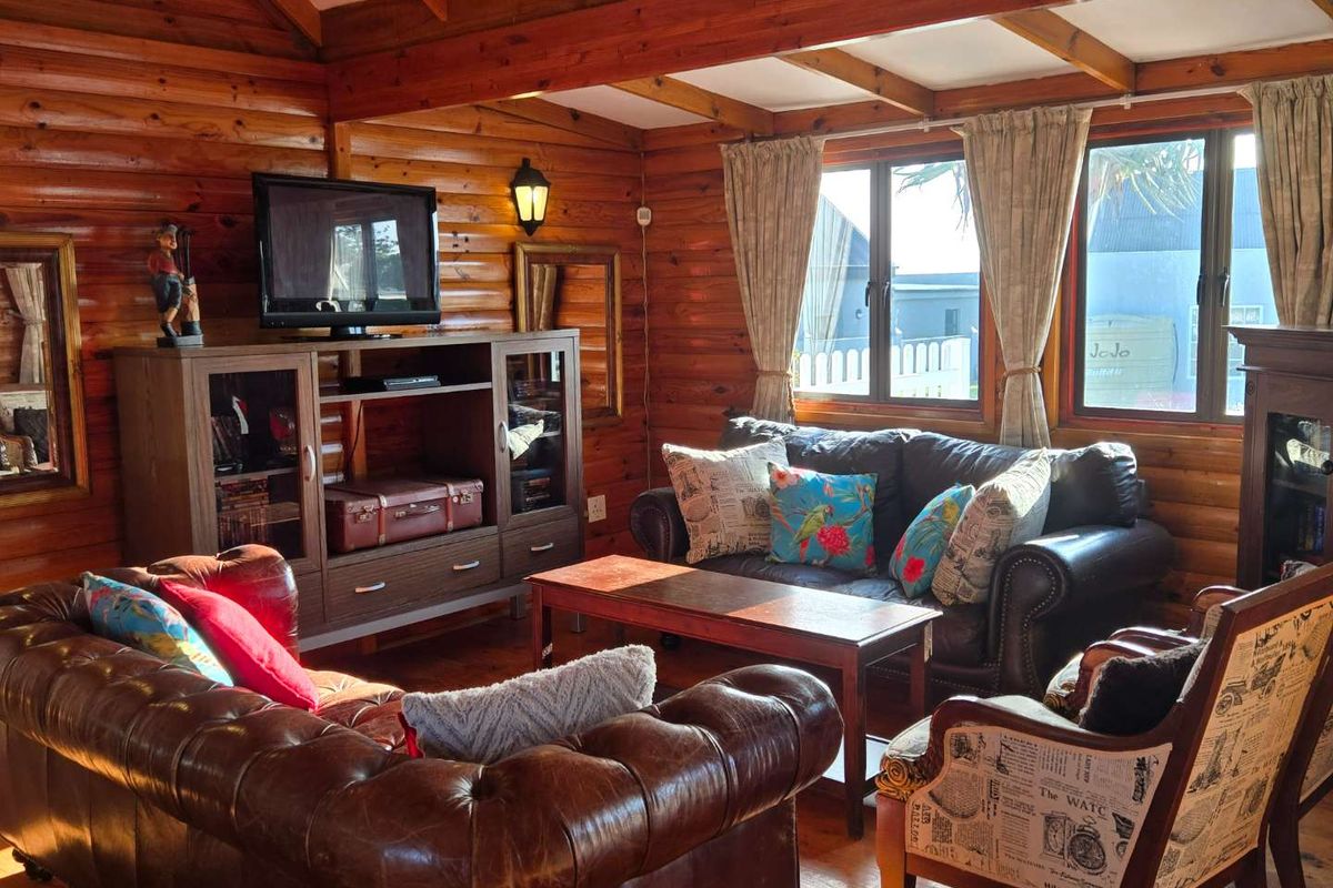 A cozy living room featuring rustic log walls, exposed timber ceiling beams, and large windows that provide natural light.