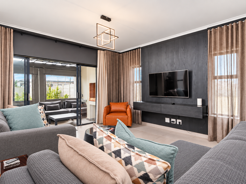 Modern living room featuring a dark wood feature wall with a floating media console, large sliding glass doors, and contemporary lighting.