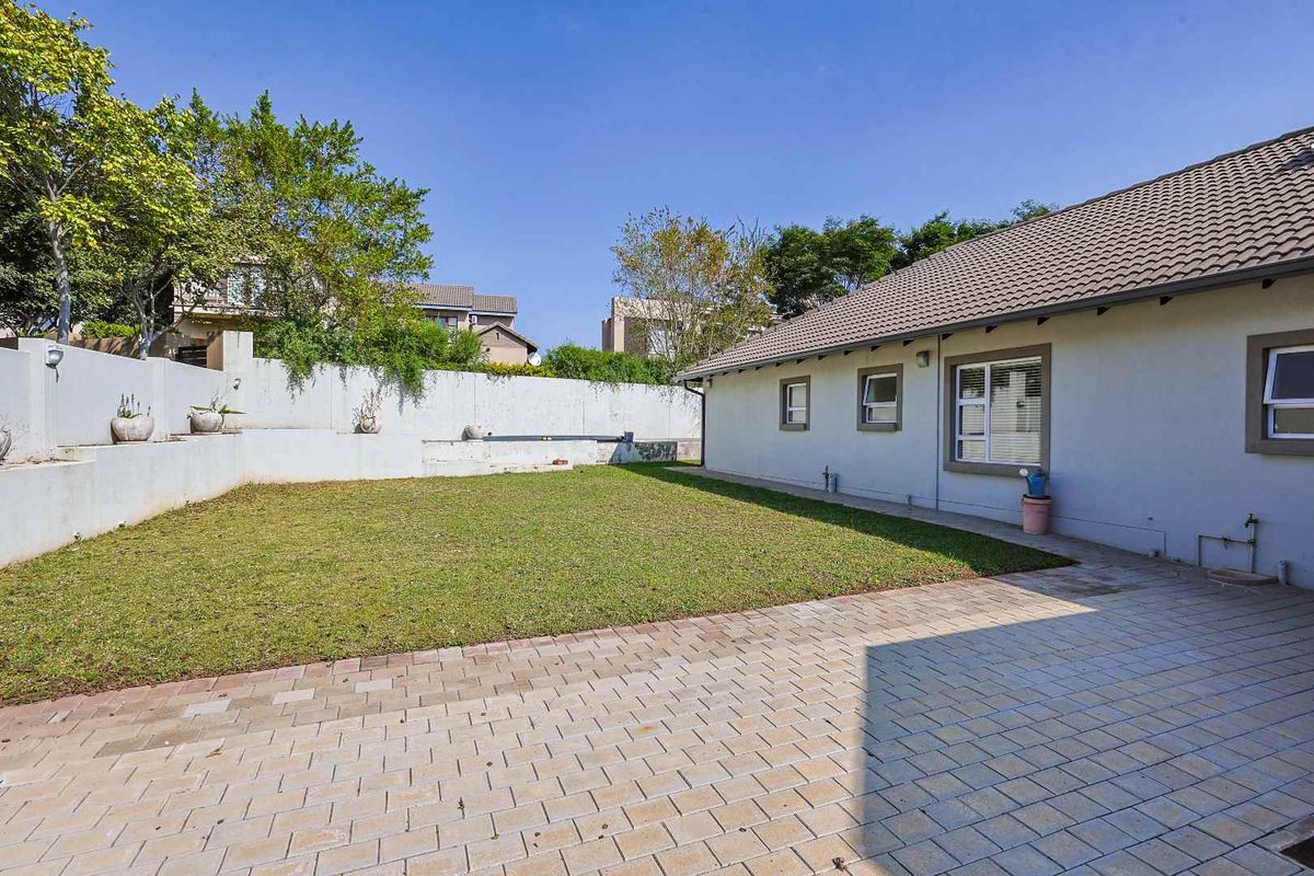 A private rear garden featuring a paved patio area, a well-maintained lawn, and a concrete retaining wall boundary.