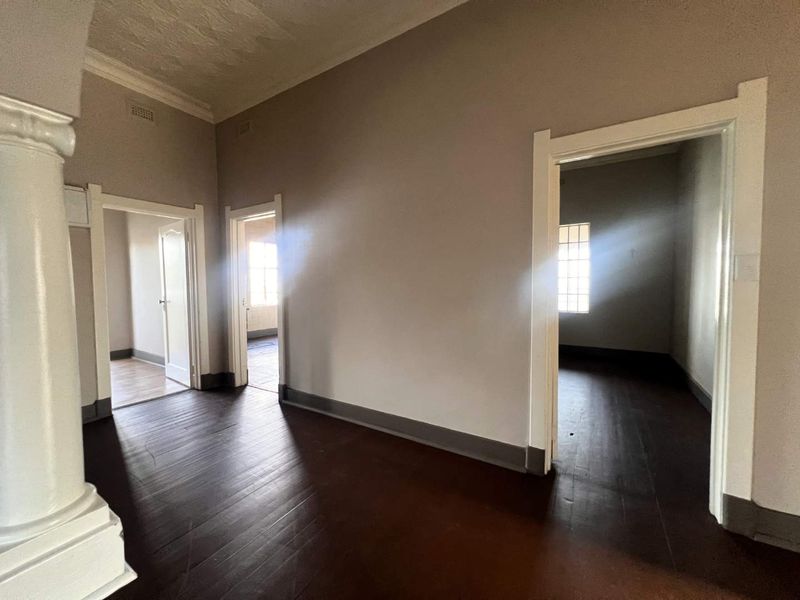 A spacious, empty hallway featuring dark timber flooring, decorative column, and classic architectural detailing, providing access to multiple rooms.
