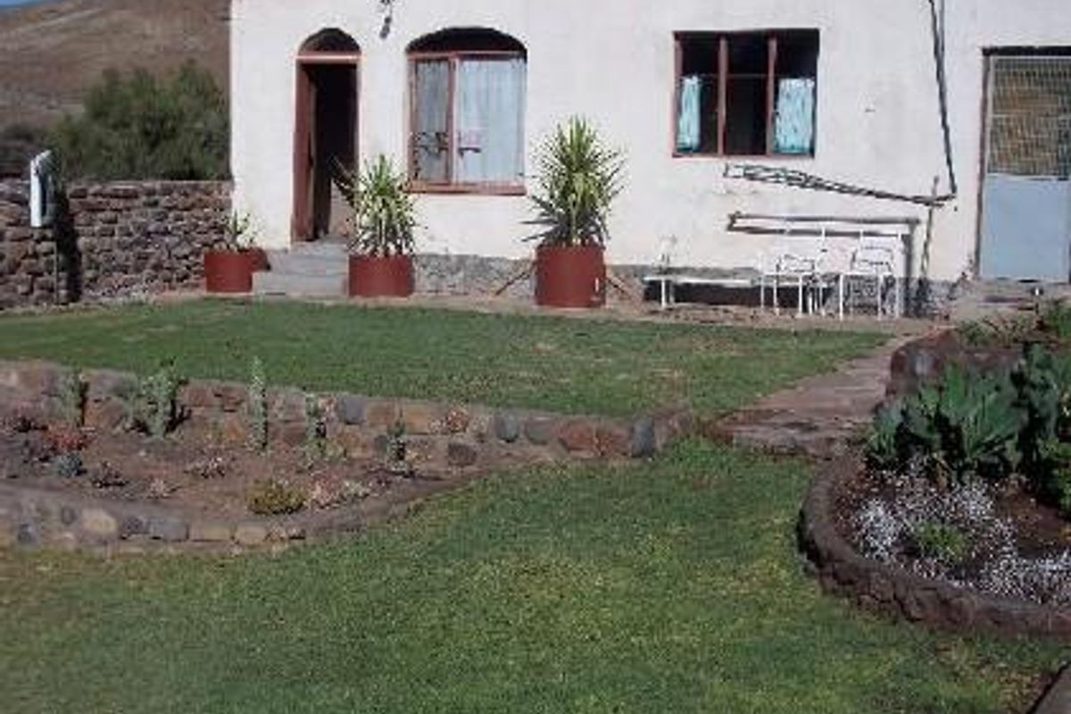 Rear view of a farm dwelling featuring a landscaped garden with stone-walled flower beds and a simple exterior facade.