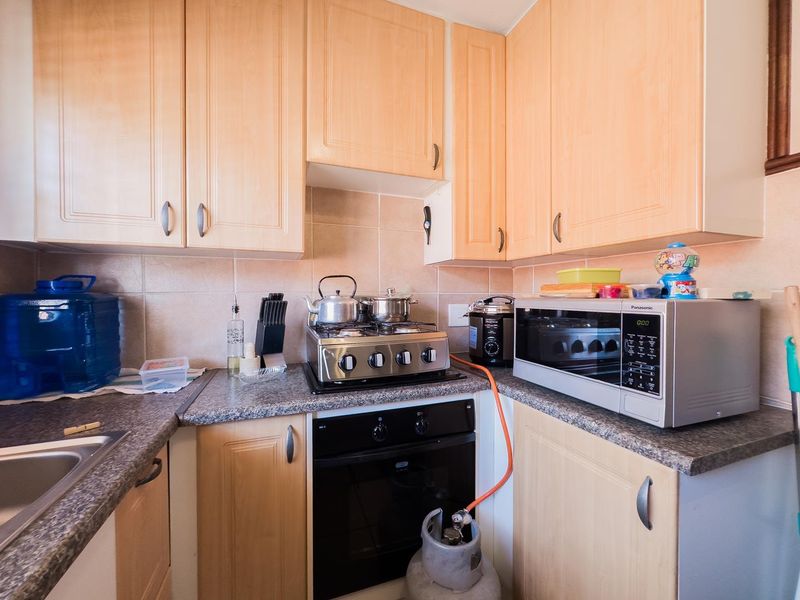 Compact kitchen featuring light wood-finish cabinetry, laminate countertops, a built-in oven, gas hob, and tiled backsplash.