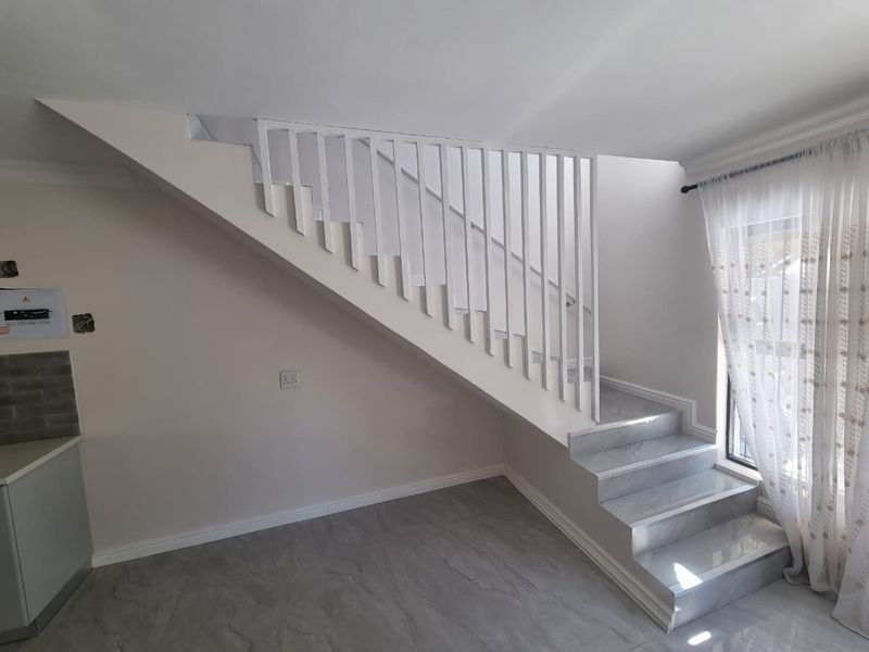 A bright, modern living area featuring a clean white staircase with metal balustrades and contemporary grey tiled flooring throughout.