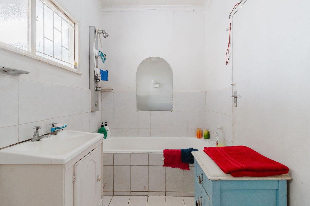 A functional bathroom featuring a built-in bathtub, vanity cabinet, and tiled finishes, offering potential for modernization and cosmetic updates.