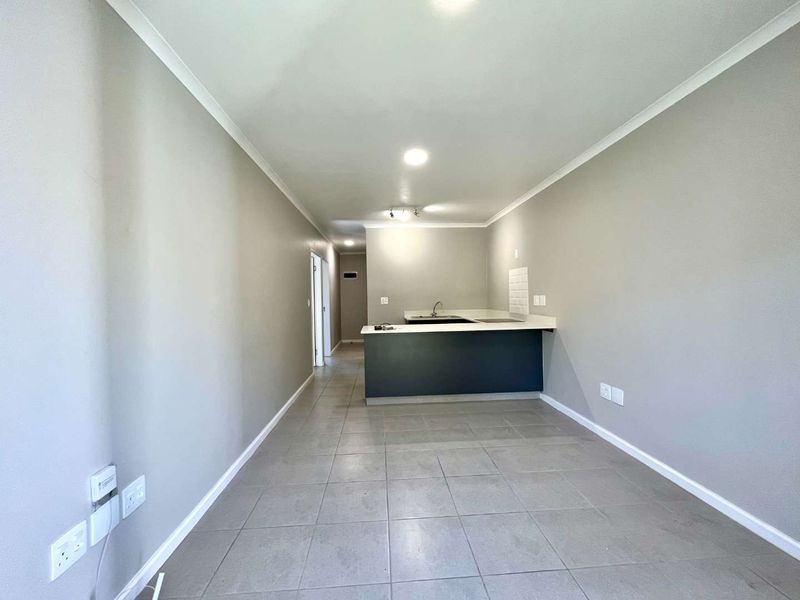 An open-plan living and kitchen area featuring neutral grey walls, tiled flooring, and a functional kitchen island with a built-in sink.