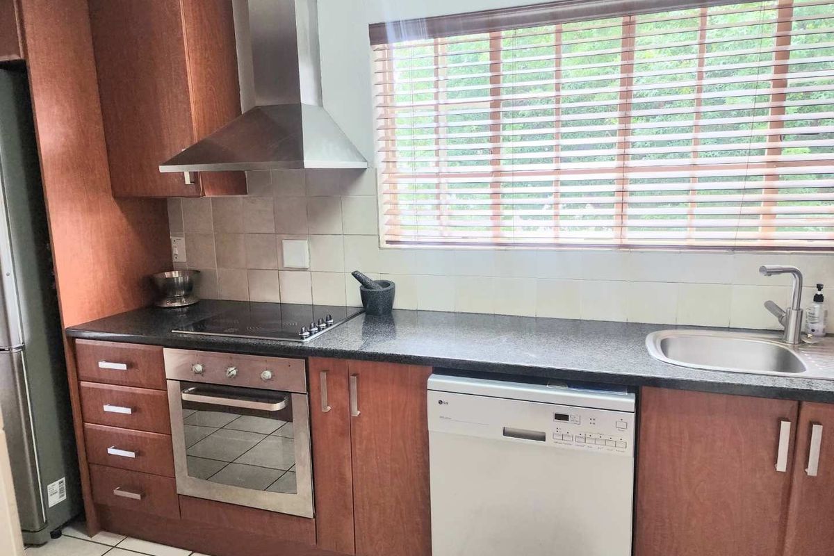 A functional kitchen featuring wood-finish cabinetry, granite countertops, a built-in oven with electric hob, and a stainless steel extractor fan.