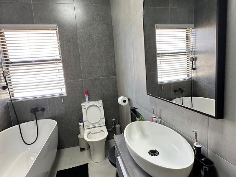 Modern bathroom featuring a sleek freestanding bathtub, vessel sink on a vanity cabinet, and contemporary grey wall tiling.