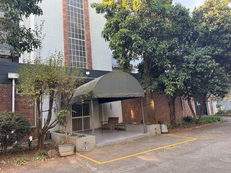 Front entrance of the apartment building featuring a brick facade, a covered porch area with a security gate, and a paved driveway.