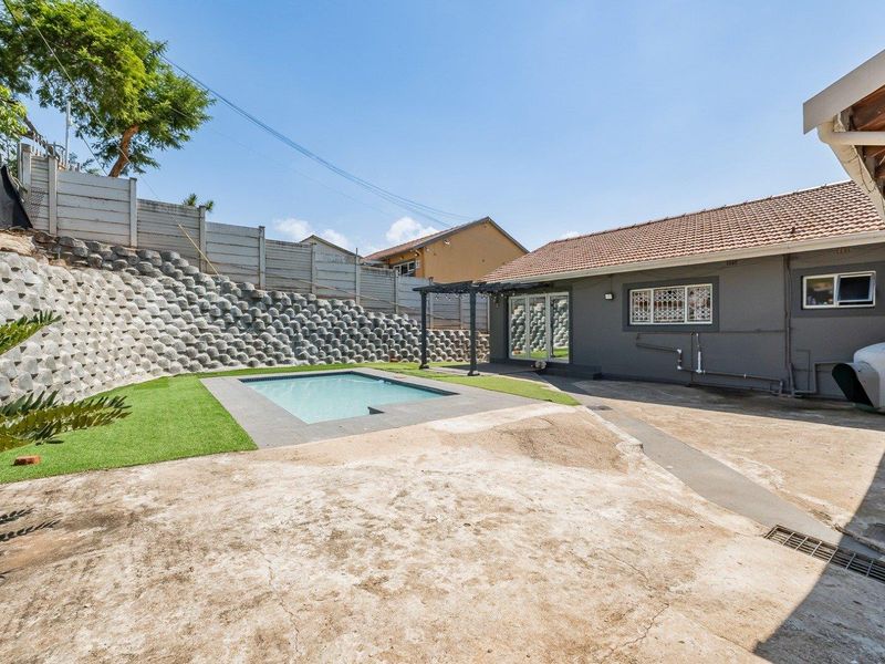 Rear exterior view featuring a swimming pool, concrete patio area, and a large retaining wall structure.