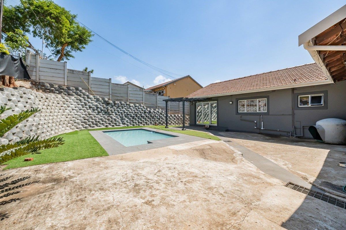 Rear exterior view featuring a swimming pool, concrete patio area, and a large retaining wall structure.