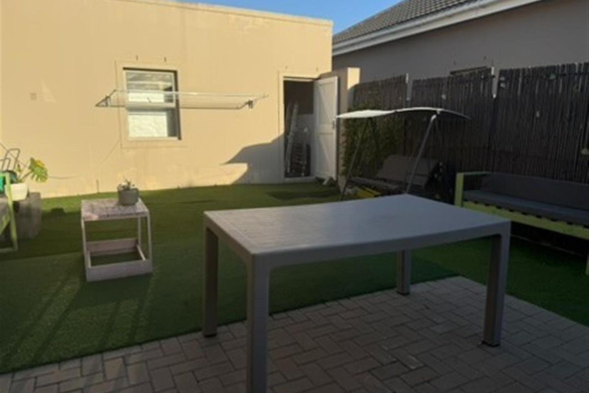 A private rear courtyard featuring paved patio area, artificial lawn, and wall-mounted drying rack, providing a low-maintenance outdoor space.