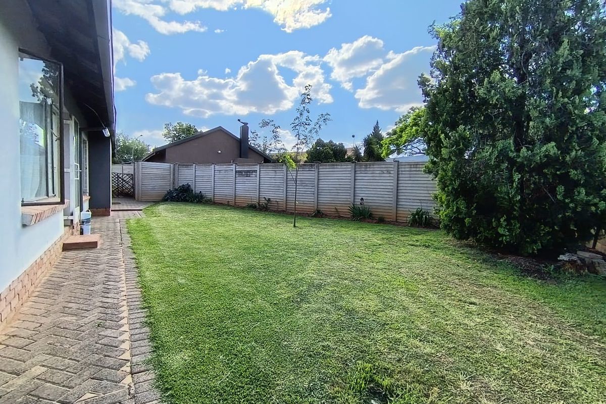 A spacious rear garden featuring a well-maintained lawn, a paved walkway along the house exterior, and secure precast concrete boundary walling.
