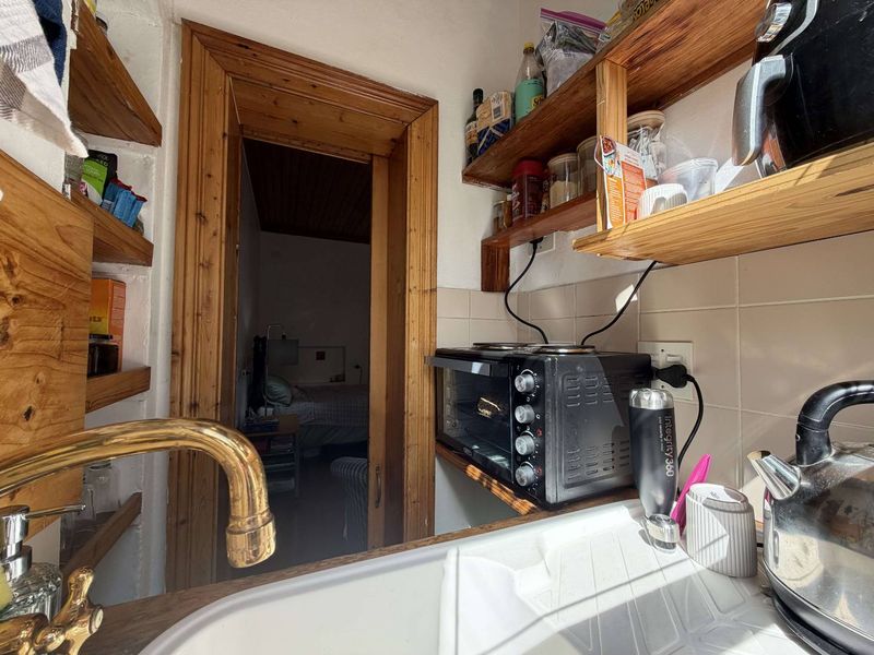 A compact scullery area featuring a sink with a brass faucet, tiled backsplash, and built-in wooden shelving, providing functional prep space.