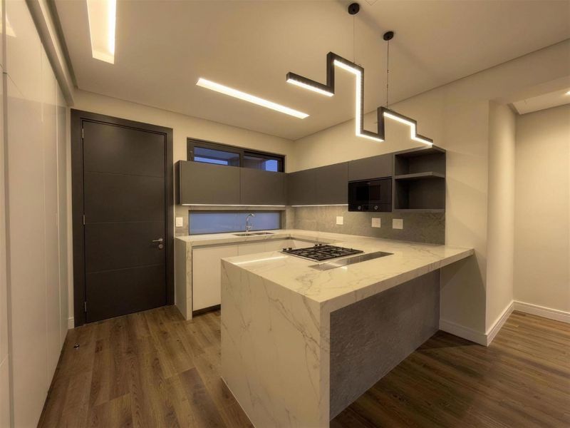 Modern kitchen featuring a marble-look stone island with a built-in gas hob, sleek cabinetry, and contemporary pendant lighting.