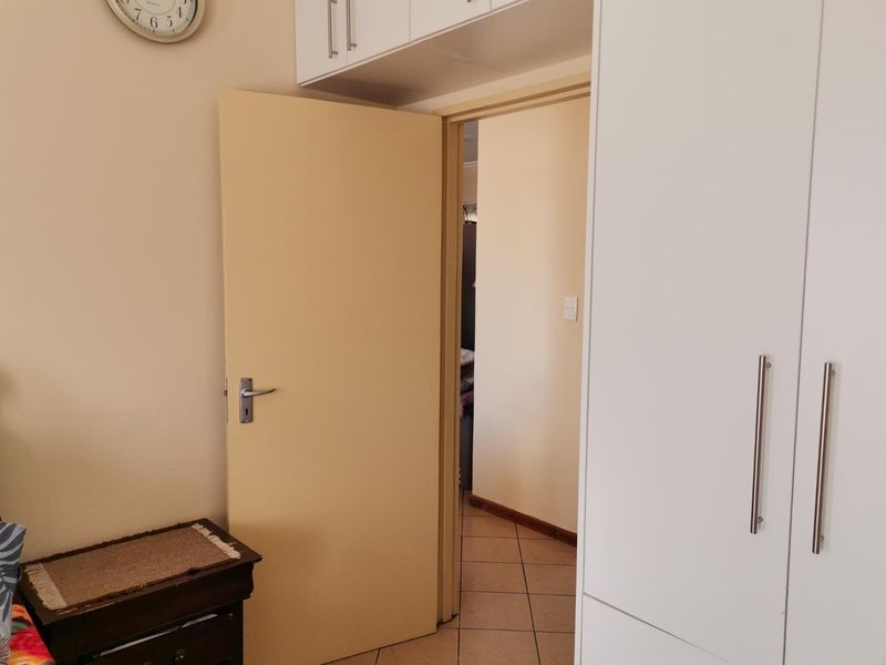 A bedroom interior featuring built-in white cupboards with overhead storage and tiled flooring, leading into an adjacent hallway.