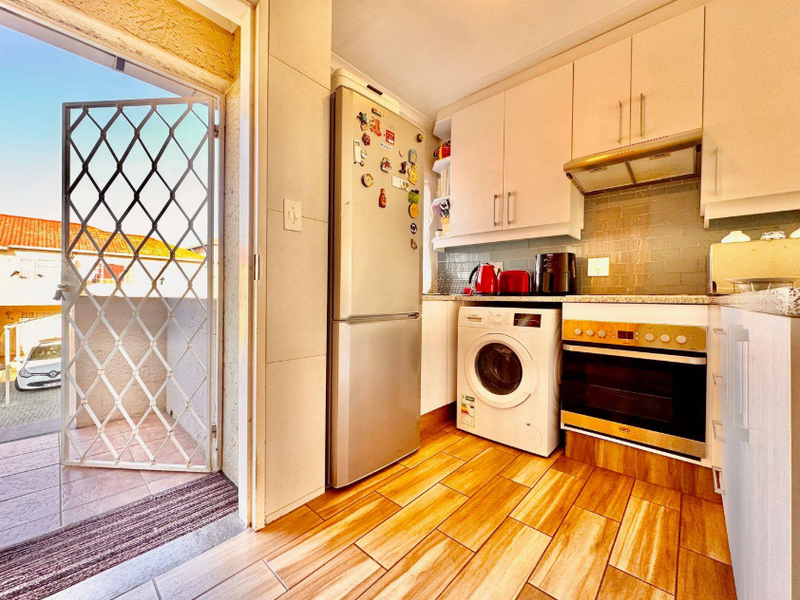 Compact kitchen featuring built-in cabinetry, integrated oven and hob, extractor fan, and tiled flooring, with direct access to an outdoor balcony area.