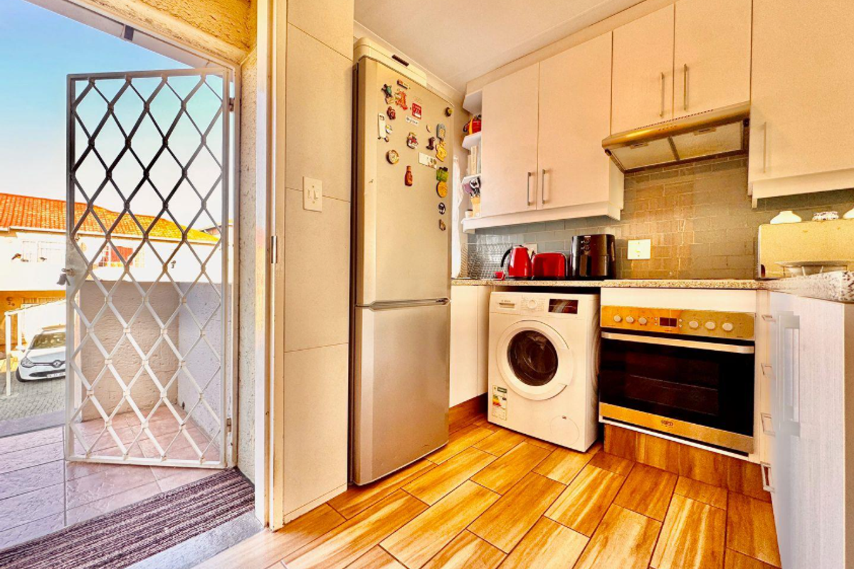 Compact kitchen featuring built-in cabinetry, integrated oven and hob, extractor fan, and tiled flooring, with direct access to an outdoor balcony area.