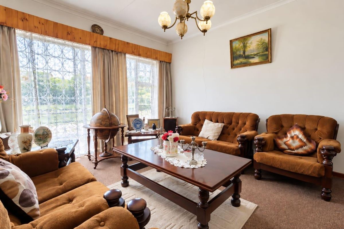 A traditional living room featuring a large sliding glass door with security gate, timber pelmet detailing, and a classic chandelier.