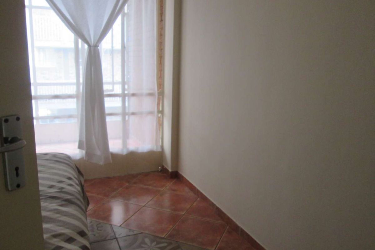 A bedroom featuring tiled flooring and a large window providing natural light, with access to an adjacent balcony area.