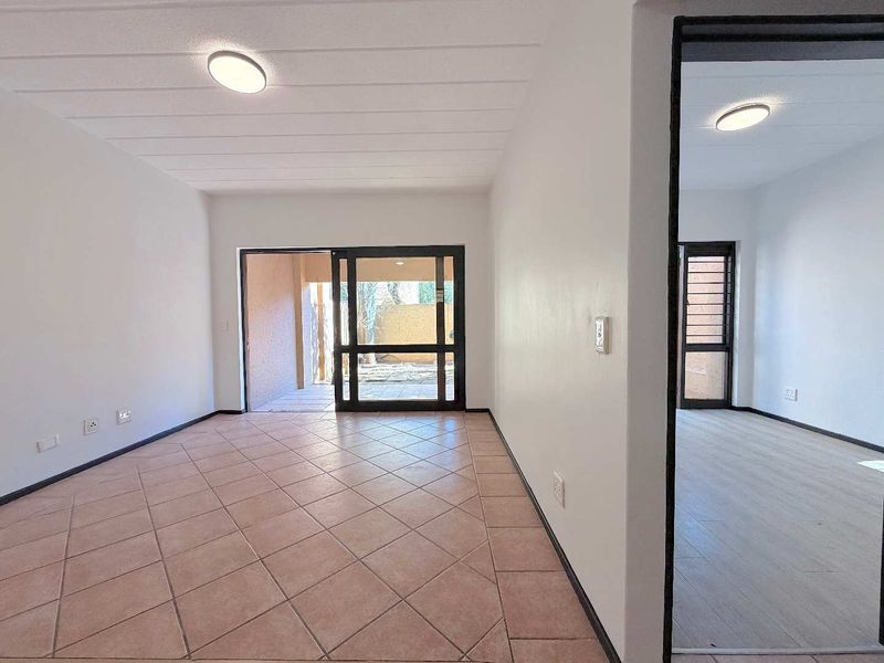 An empty, well-lit living area featuring neutral tiled flooring, a sliding glass door leading to an outdoor space, and clean white walls.
