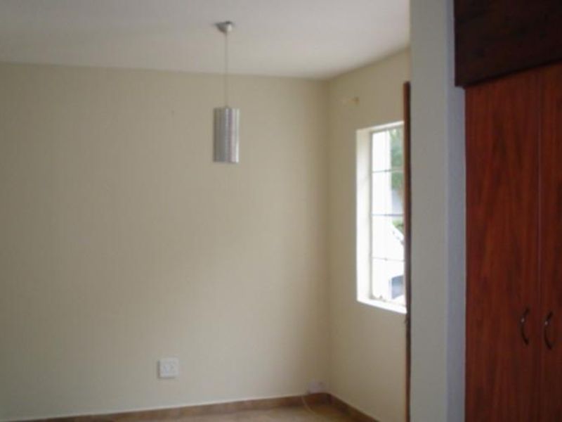 A simple, empty bedroom featuring tiled flooring, a built-in wooden wardrobe, and a window with security bars.