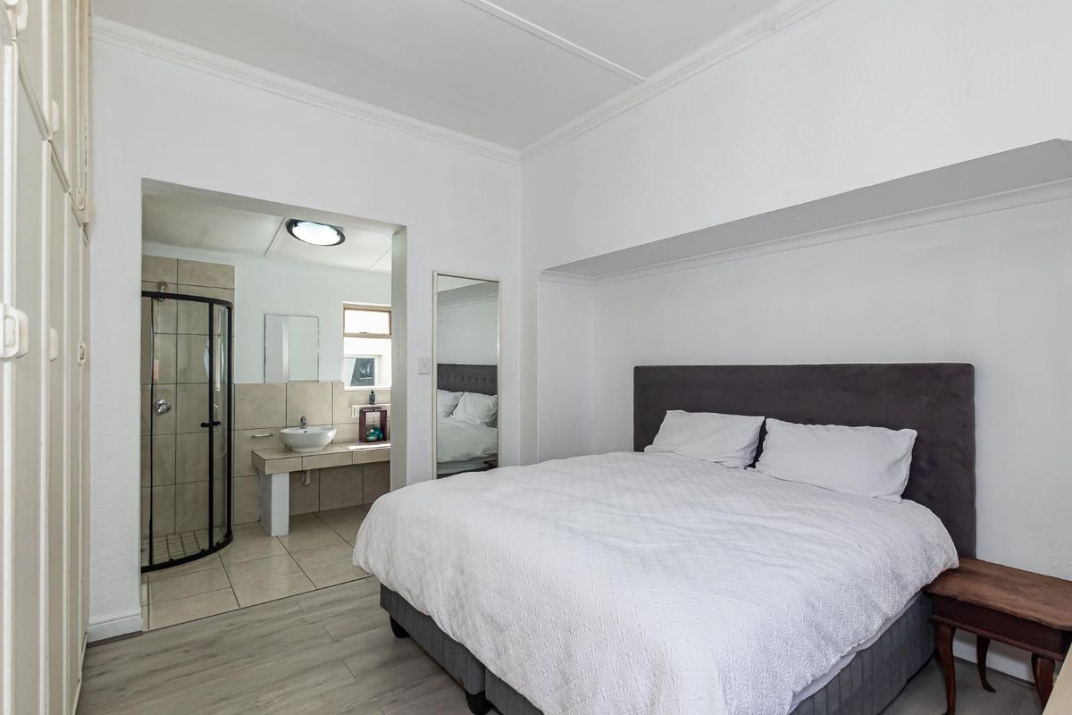 A bedroom featuring light wood-look flooring and an en-suite bathroom with a corner shower and a vessel sink vanity.