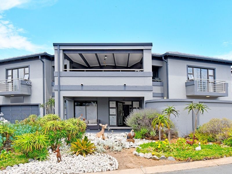 A modern double-storey residential property featuring a grey facade, multiple balconies, a covered patio, and a well-maintained landscaped front garden.