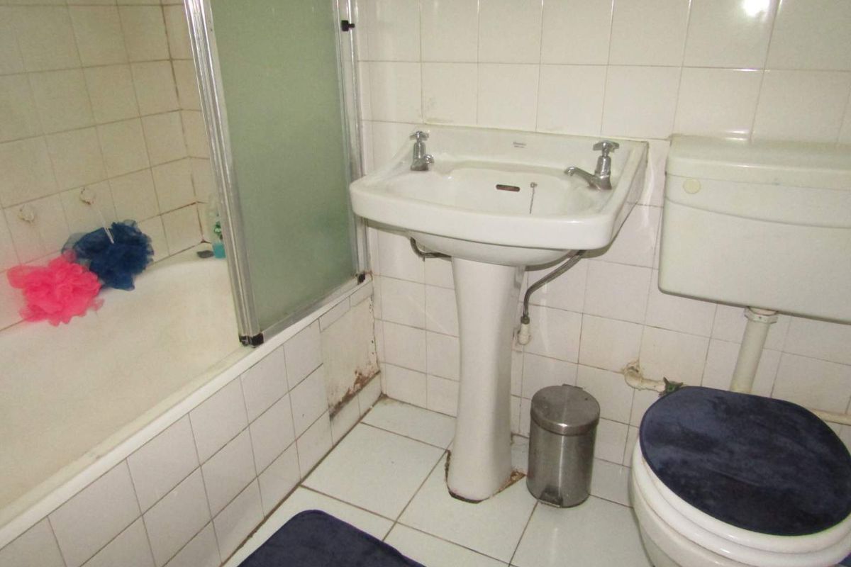 A dated bathroom featuring a pedestal sink, a toilet, and a shower-over-bath combination with tiled walls and flooring.