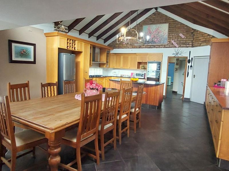 Spacious open-plan kitchen and dining area featuring vaulted ceilings with exposed timber beams, brick accents, and extensive built-in cabinetry.