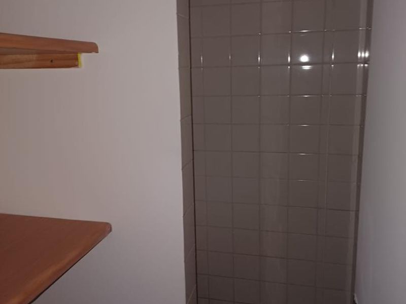 A compact shower area featuring tiled walls and mosaic flooring, complemented by built-in shelving for storage.