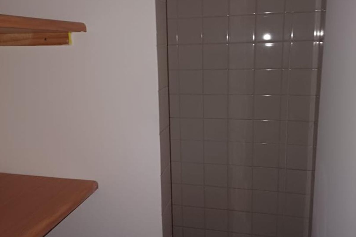 A compact shower area featuring tiled walls and mosaic flooring, complemented by built-in shelving for storage.