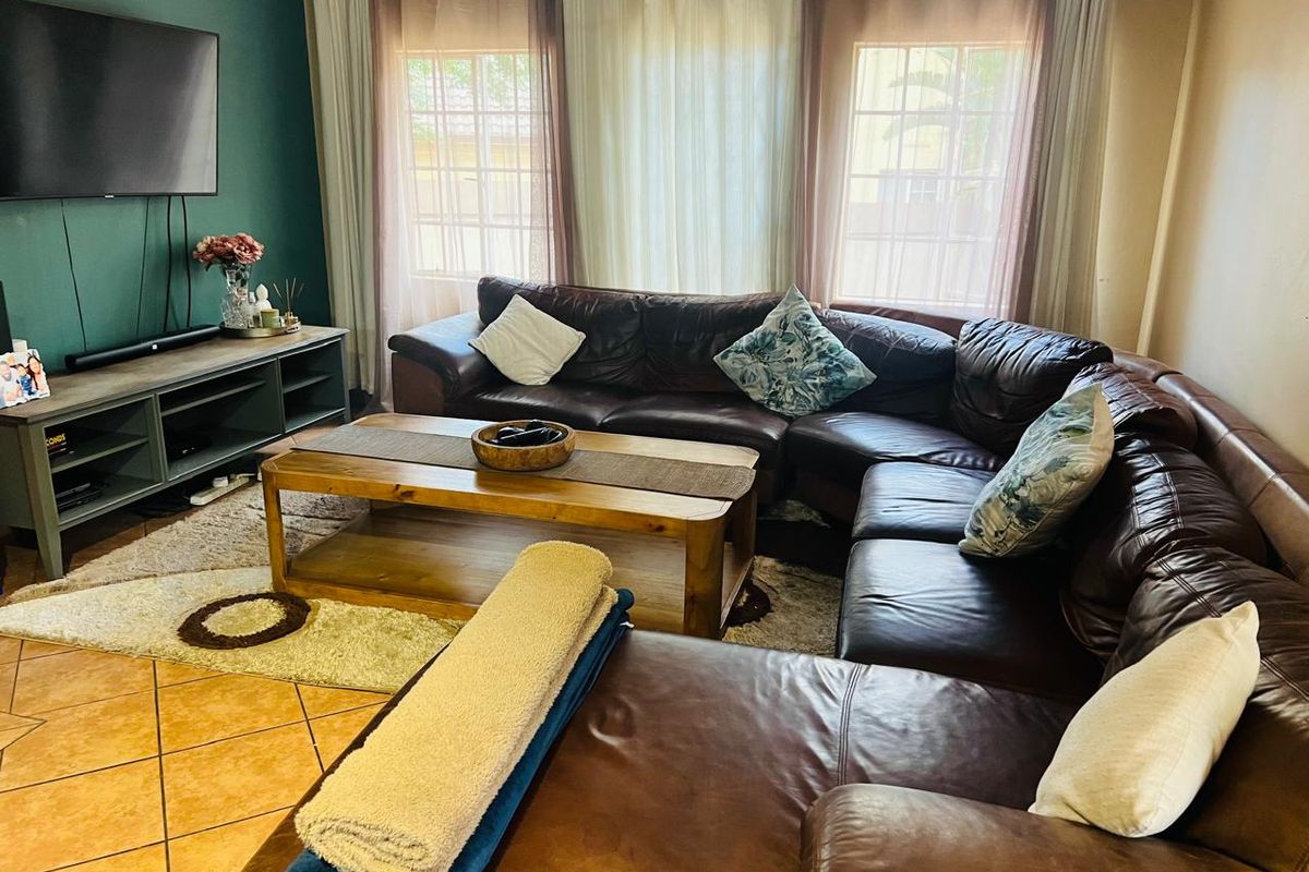 A comfortable living room featuring tiled flooring, large windows with curtains, and a dedicated accent wall for media setup.