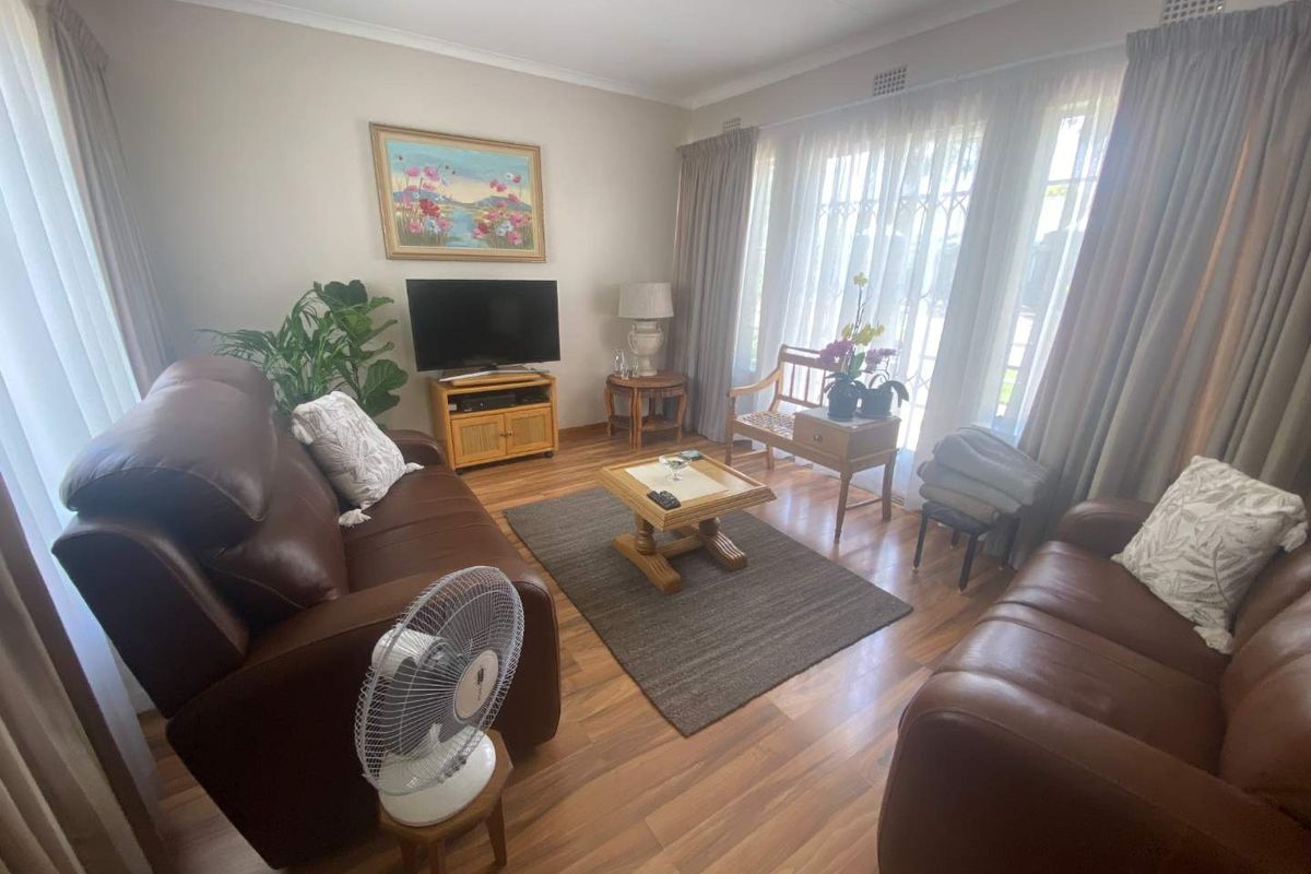 A well-maintained living room featuring wood-look laminate flooring, large windows with curtain tracks, and neutral wall finishes.