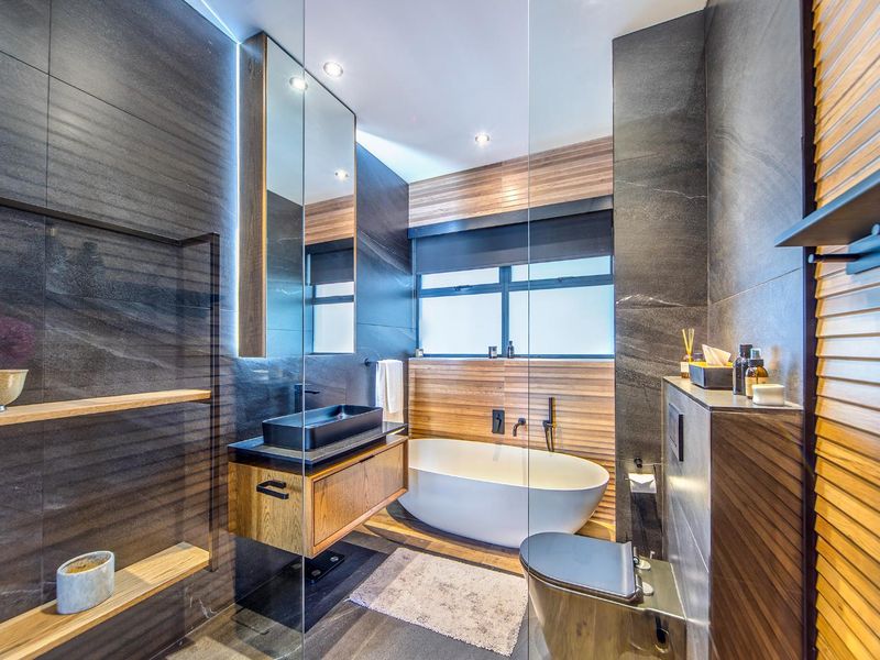 Modern, high-end bathroom featuring a freestanding bathtub, wall-mounted vanity with vessel sink, premium dark stone tiling, and wood-look accent paneling.
