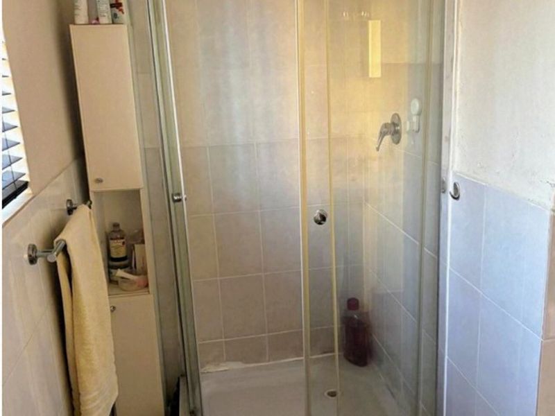 A functional bathroom featuring a corner shower enclosure with tiled walls and flooring, providing a practical space that could benefit from cosmetic updates.