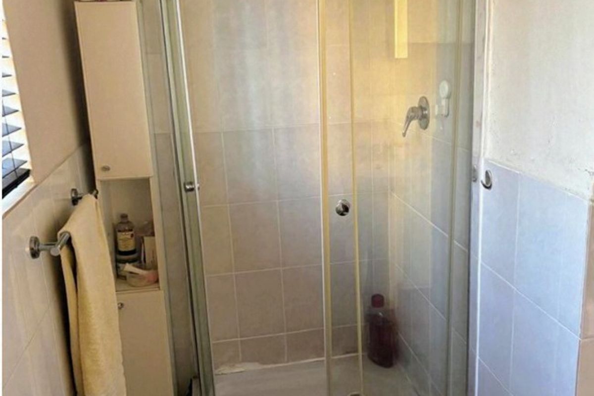 A functional bathroom featuring a corner shower enclosure with tiled walls and flooring, providing a practical space that could benefit from cosmetic updates.