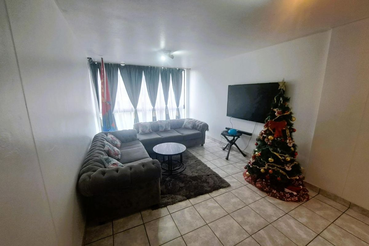 A living room featuring tiled flooring and a large window with curtains, providing a functional and neutral space for relaxation.
