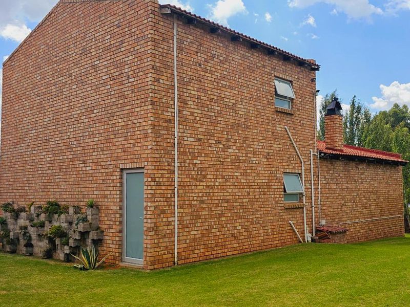A side and rear view of a face-brick small holding dwelling featuring a tiled roof, chimney, and integrated garden planter wall.
