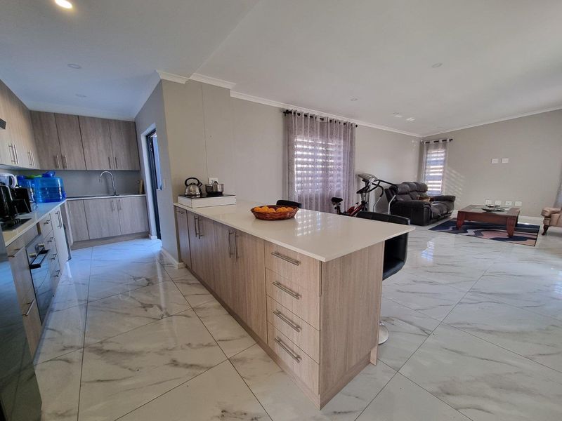 Spacious open-plan living area featuring a modern kitchen with a central island, quartz countertops, and sleek marble-look floor tiles throughout.